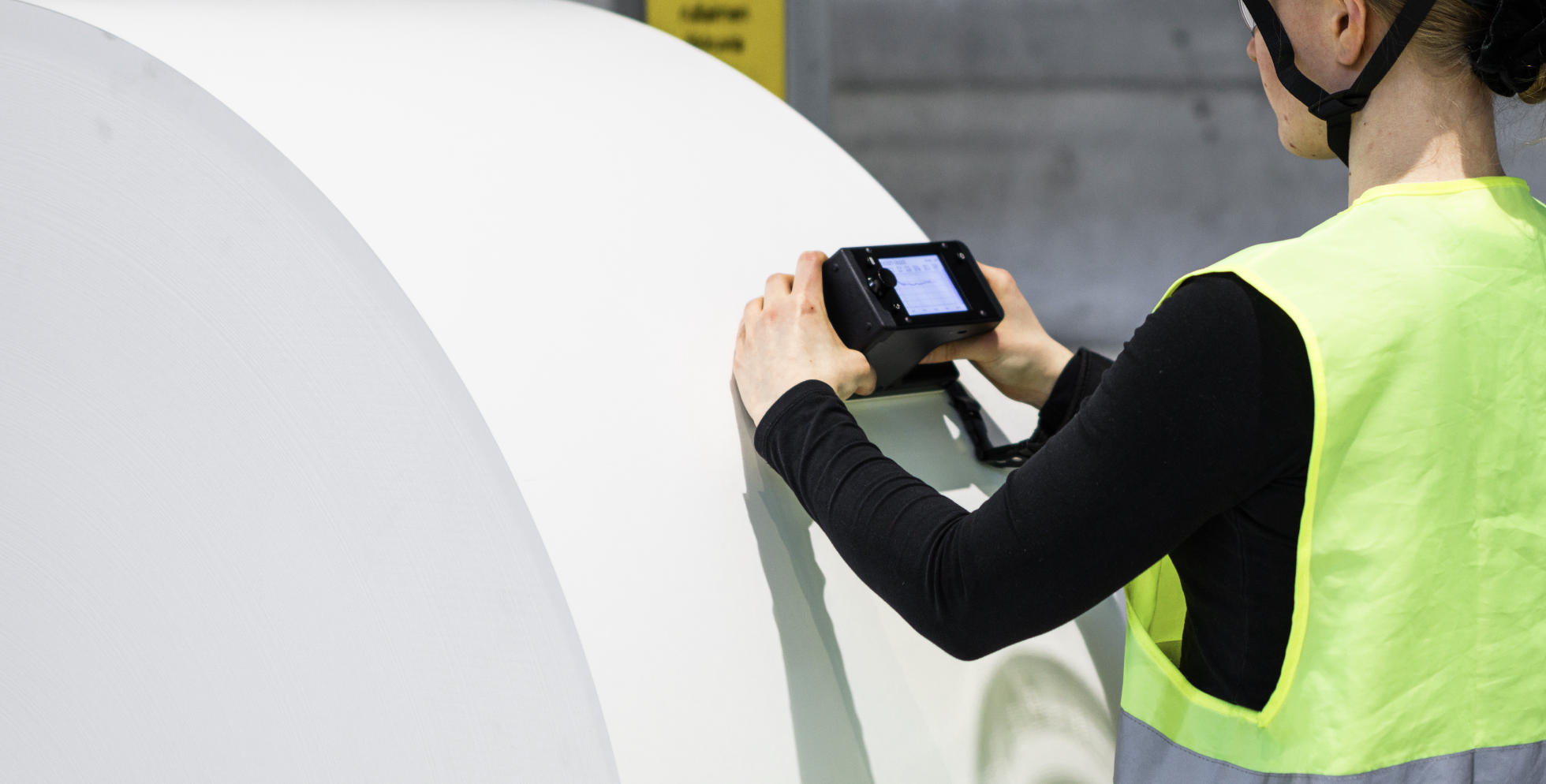 An operator holding the RQP Live handheld roll hardness profiler next to a paper roll, preparing to take a measurement.