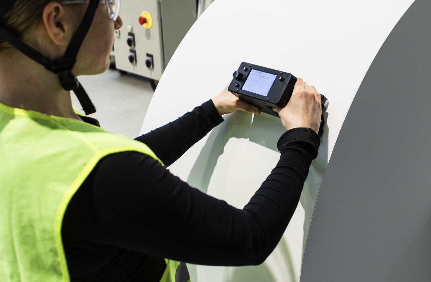 A person in a high-visibility vest measuring the hardness of a large paper roll using the Tapio RQP Live handheld device.