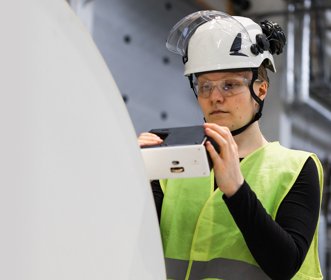 An operator holding the RQP Live handheld roll hardness profiler next to a paper roll, preparing to take a measurement.