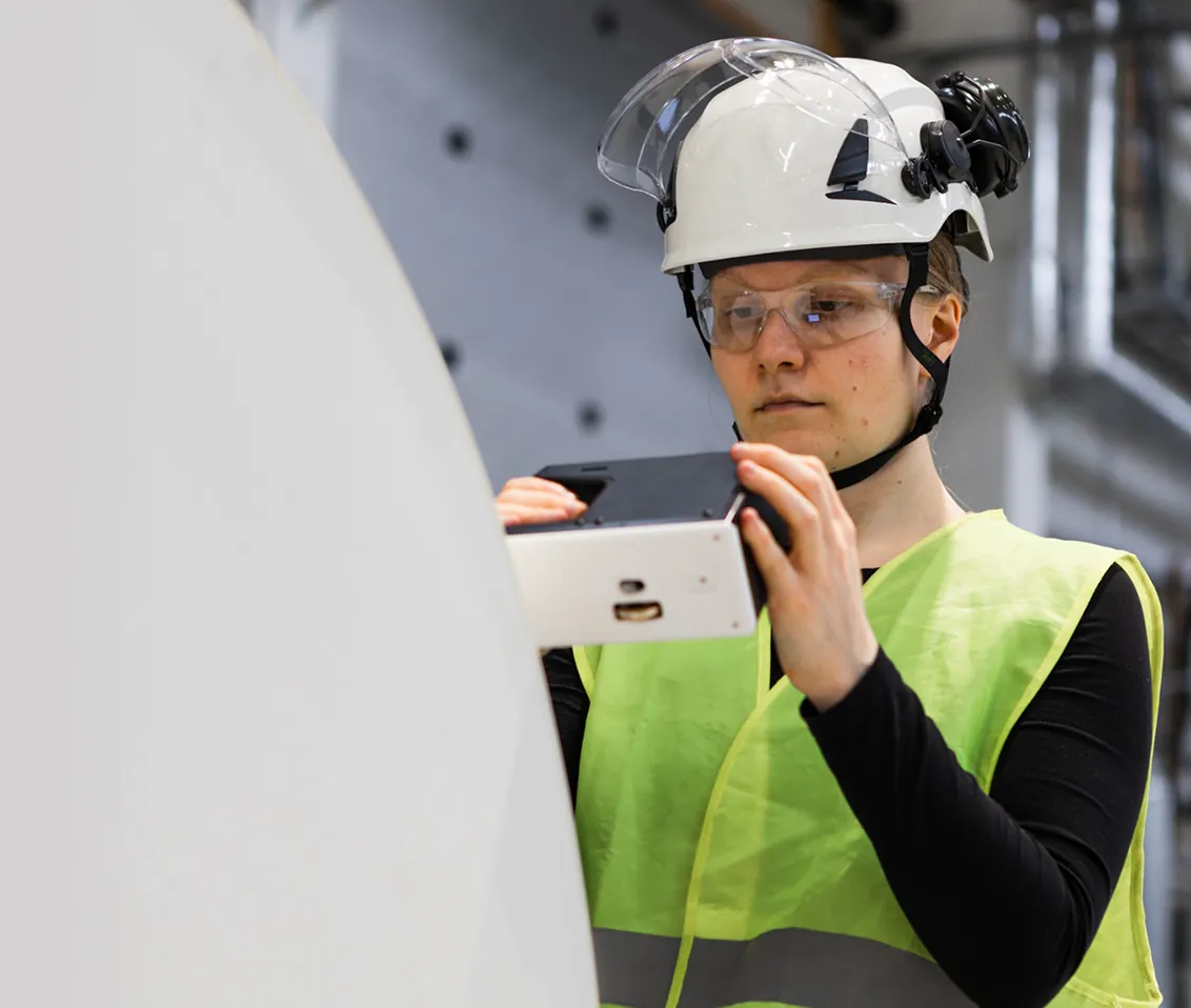 An operator holding the RQP Live handheld roll hardness profiler next to a paper roll, preparing to take a measurement.