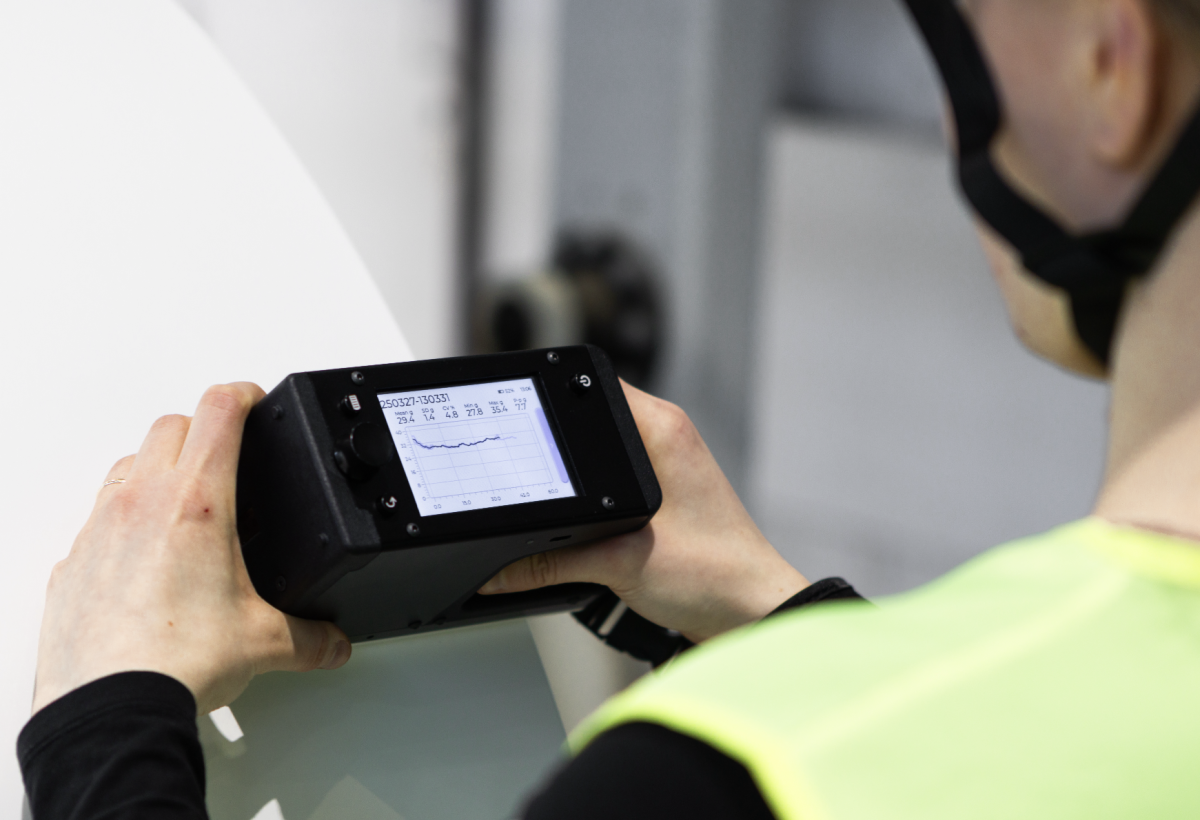 An operator holding the RQP Live handheld roll hardness profiler next to a paper roll, preparing to take a measurement.
