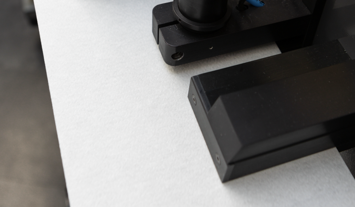 Close-up of the Tapio Caliper sensor measuring the thickness of a paper sheet as it passes between two black sensor modules.