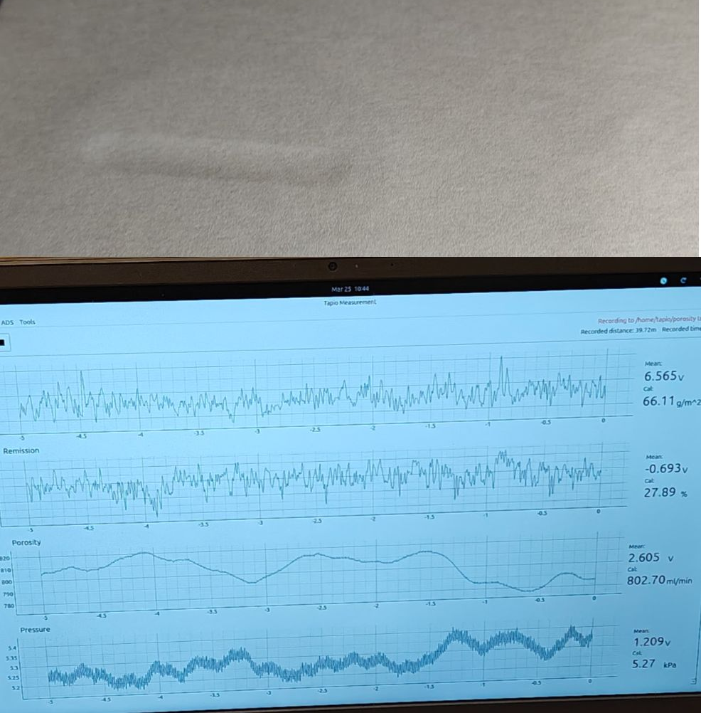 Paper sheet on a measurement device with a screen displaying porosity, pressure and signal graphs.