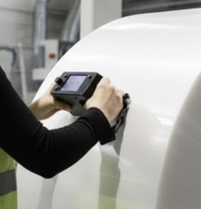 Technician using a handheld measurement device on a large plastic roll surface in an industrial environment