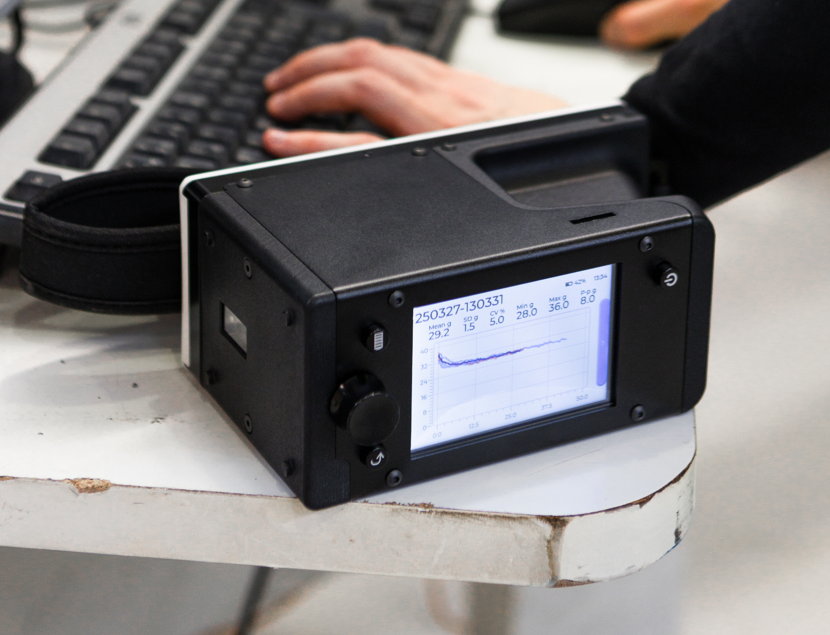 Tapio RQP Live handheld roll hardness profiler on a table displaying a hardness profile and statistics on its screen.